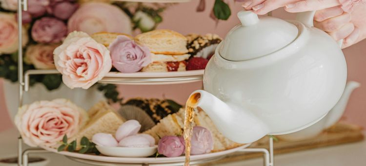 Someone pouring tea with cakes on a stand behind
