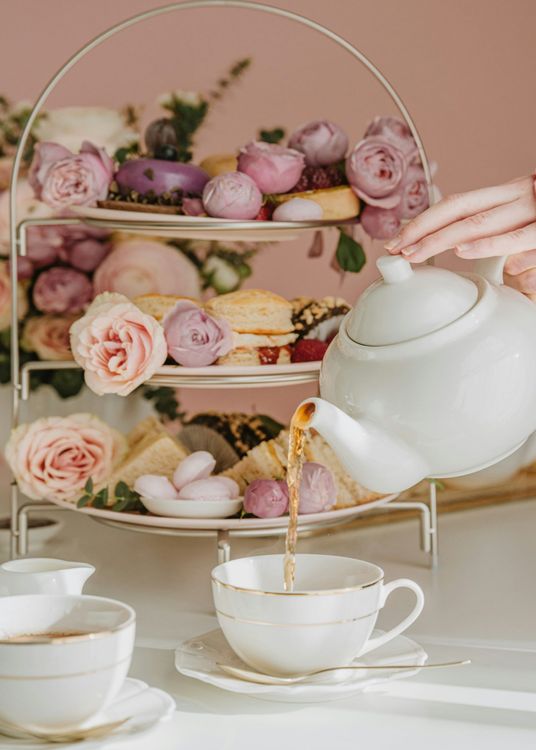 Someone pouring tea with cakes on a stand behind